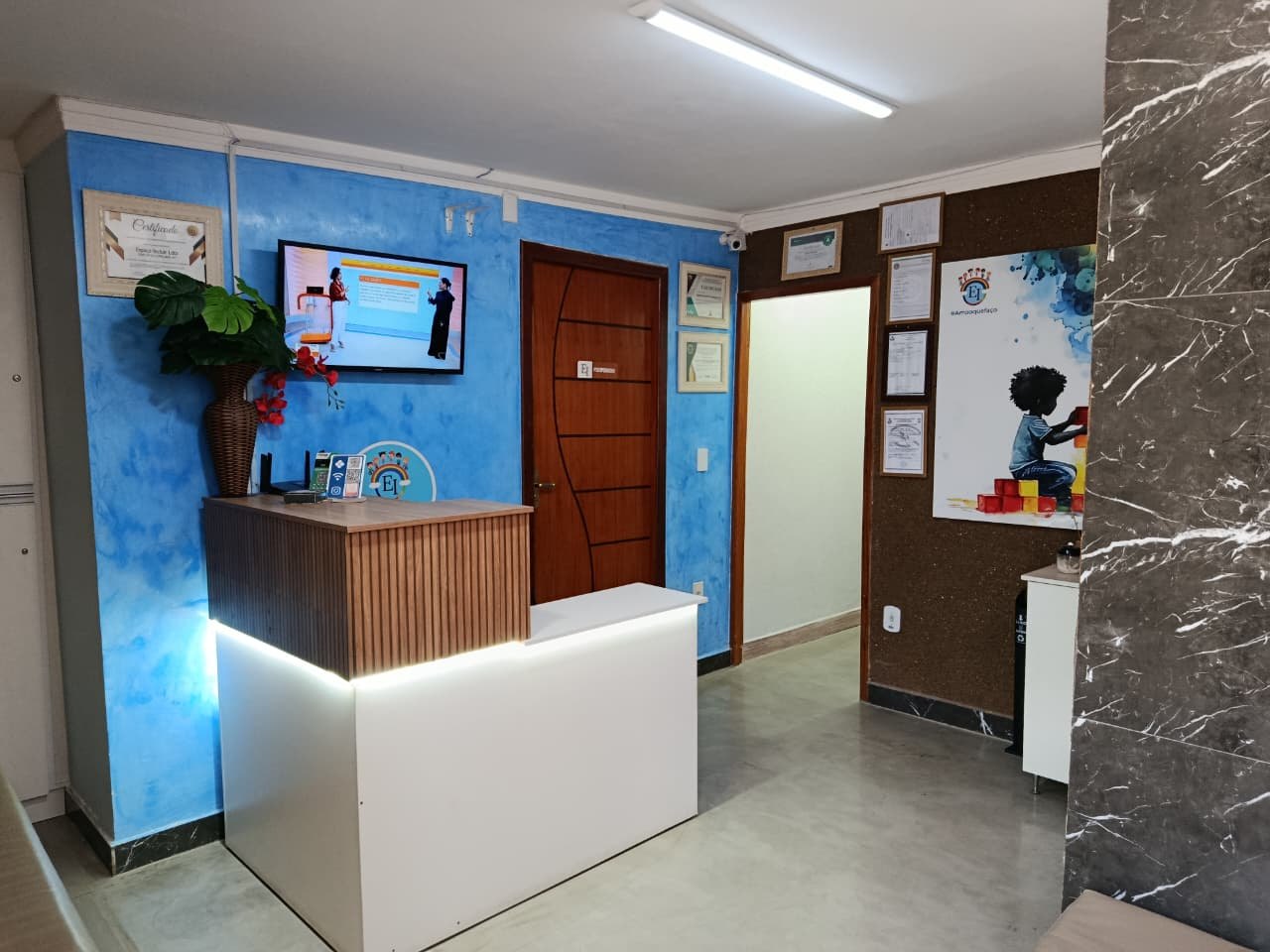 Recepção do Espaço Incluir, com balcão, certificados e o logo EI.